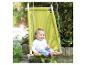 Een lachende baby zit in een groene schommel, buiten opgehangen.