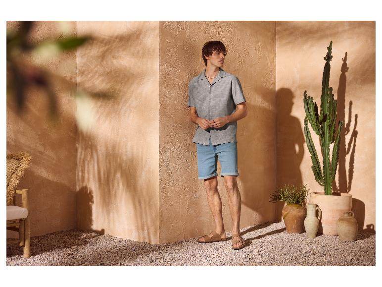 Man in overhemd met korte mouwen en denim shorts, sandalen, in een mediterrane setting.