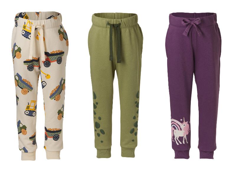 Drie kinderjoggingbroeken: een beige met vrachtwagenmotieven, een kaki met vlekken en een paarse met een eenhoorn.