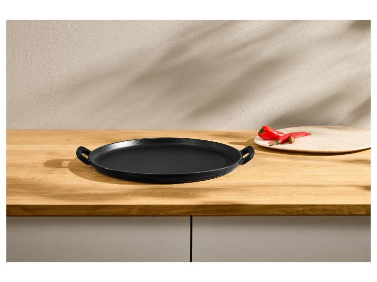 Zwarte ronde gietijzeren pan op een houten tafel met rode paprika's.