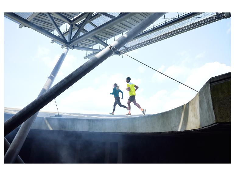 Twee hardlopers trainen op een gebogen baan, onder een metalen constructie.