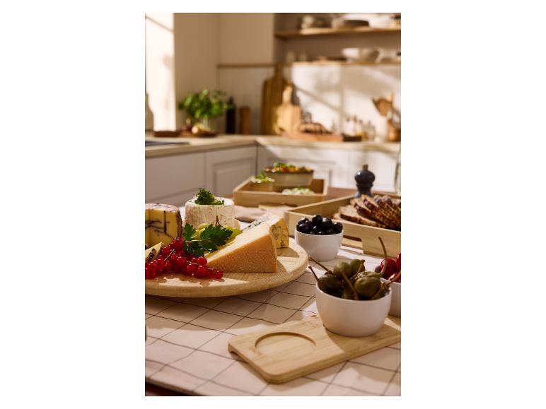 Een selectie van kazen, bessen en olijven op een keukentafel.