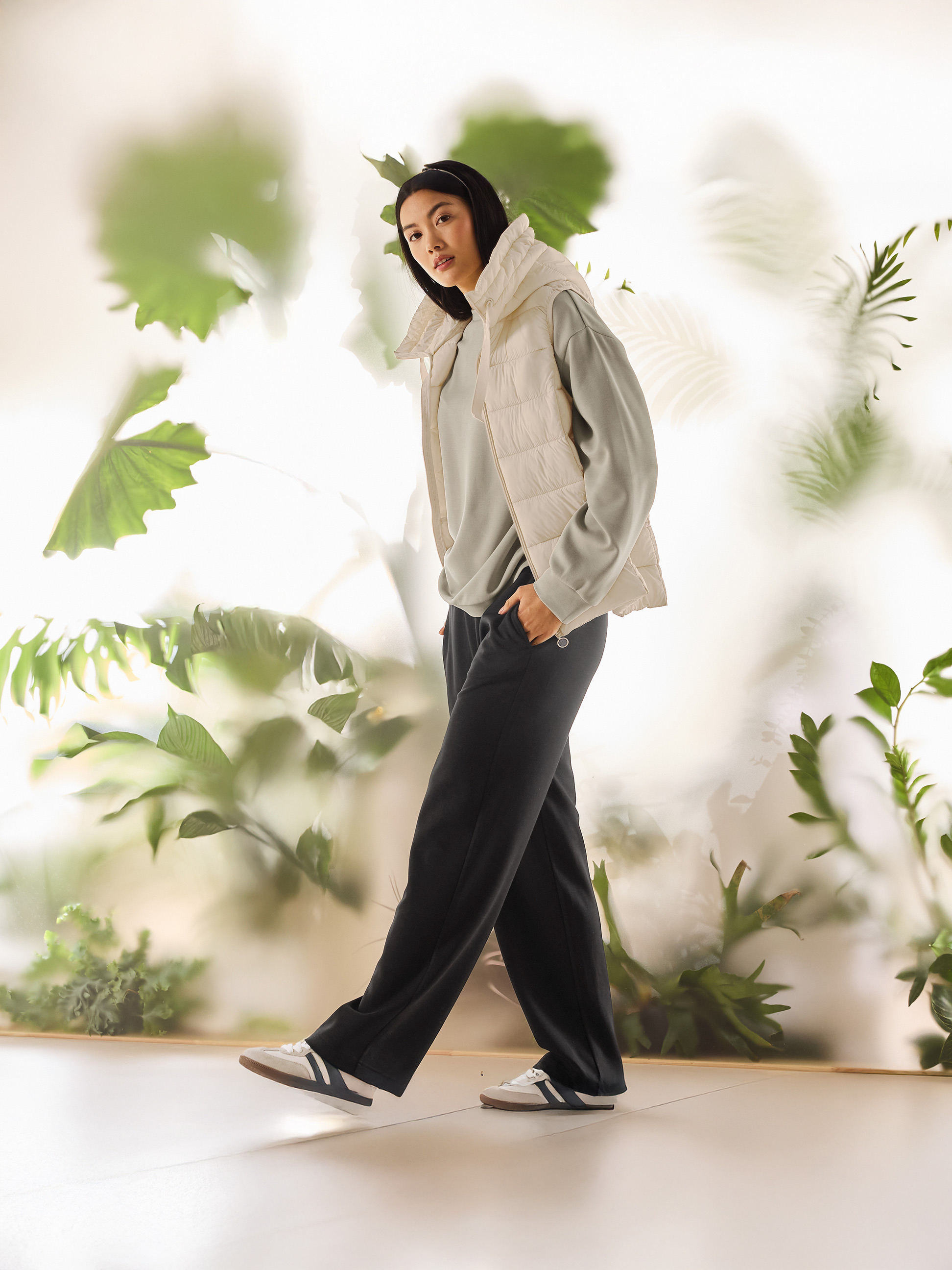 Vrouw in een beige gewatteerd vest, lichtgroene sweater en zwarte broek loopt.