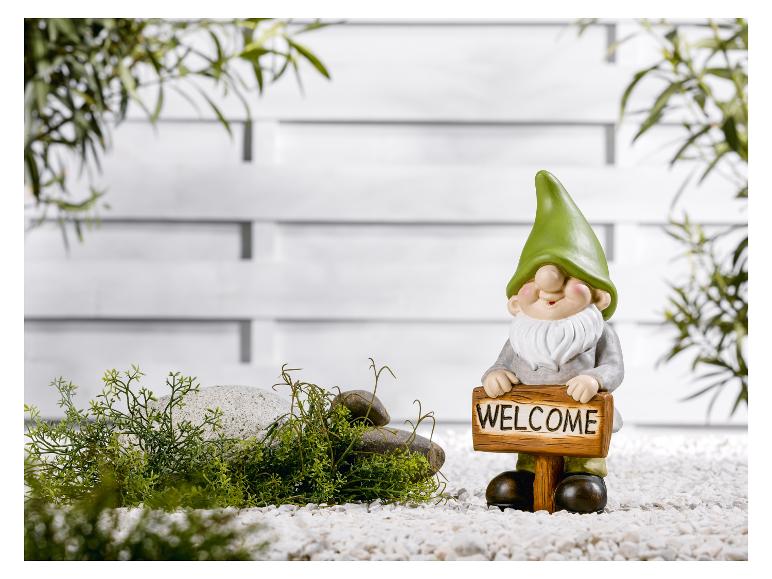 Een tuinman met een 'Welkom'-bordje, omringd door stenen en planten.