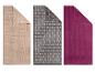 Drie badhanddoeken: beige met geometrische patronen, grijs met baksteenpatroon en een effen paarse.