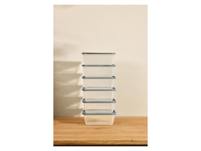 Stapel doorzichtige voedselcontainers met grijze deksels op een houten aanrecht.