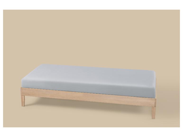 Lichtgrijs matras op een houten bedframe tegen een beige achtergrond.