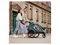 Ouders duwen een Hauck kinderwagen met een kind, lopend over straat.