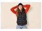 Vrouw in zwarte bodywarmer, oranje trui en muts, met handen achter het hoofd.