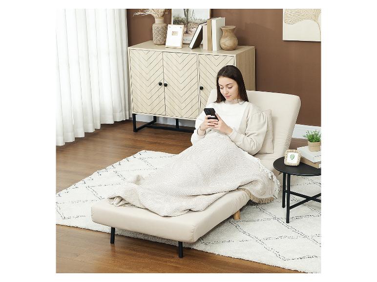 Vrouw ontspant op een beige chaise longue met een deken, gebruikt haar telefoon in een gezellige kamer.
