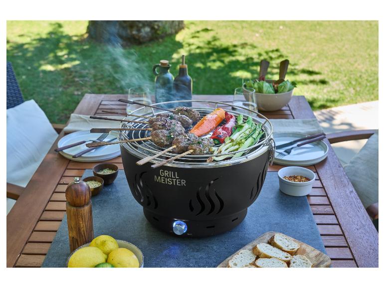Barbecue met vlees- en groentespiesjes op een buitentafel, omringd door servies en kruiden.