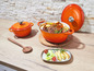 Een oranje gietijzeren braadpan met deksel, gevuld met gebakken kip en groenten.