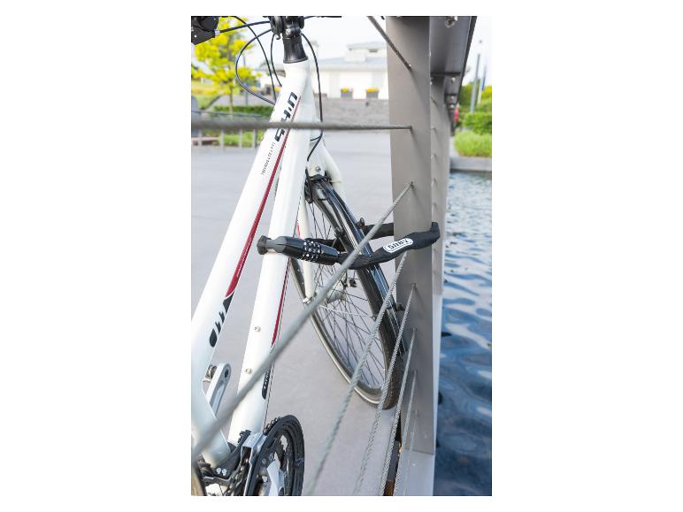 Witte trekkingfiets beveiligd met een zwart slot aan een metalen reling boven water.
