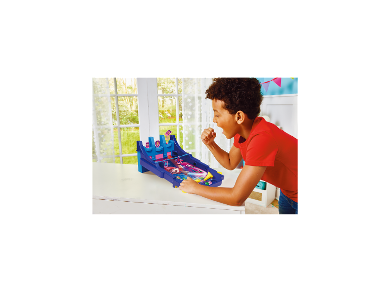 Een jongen speelt flipperkast op een witte tafel, met een raam op de achtergrond.