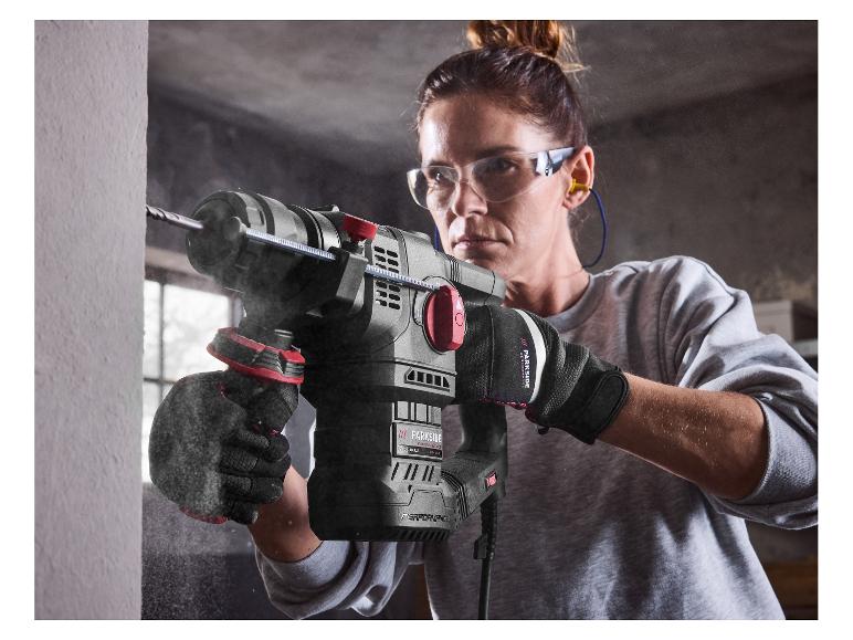 Vrouw in veiligheidsuitrusting gebruikt een Parkside Performance boorhamer op een muur.