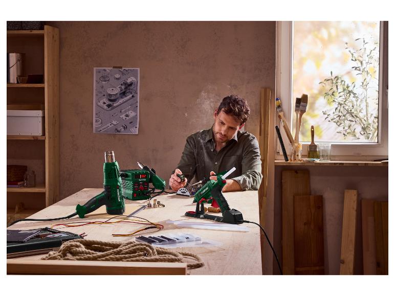 Man gebruikt Parkside soldeerbout en lijmpistool aan een werkbank.