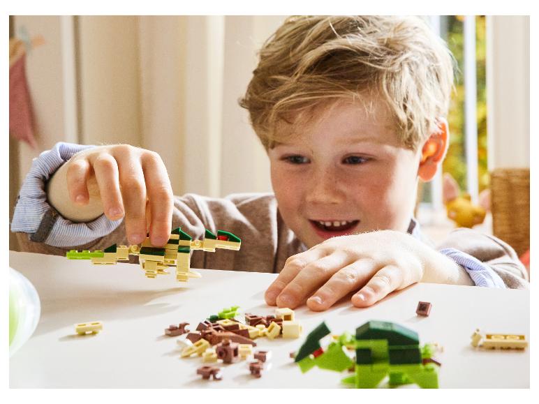 Een lachend kind speelt met dinosaurusvormig constructiespeelgoed.