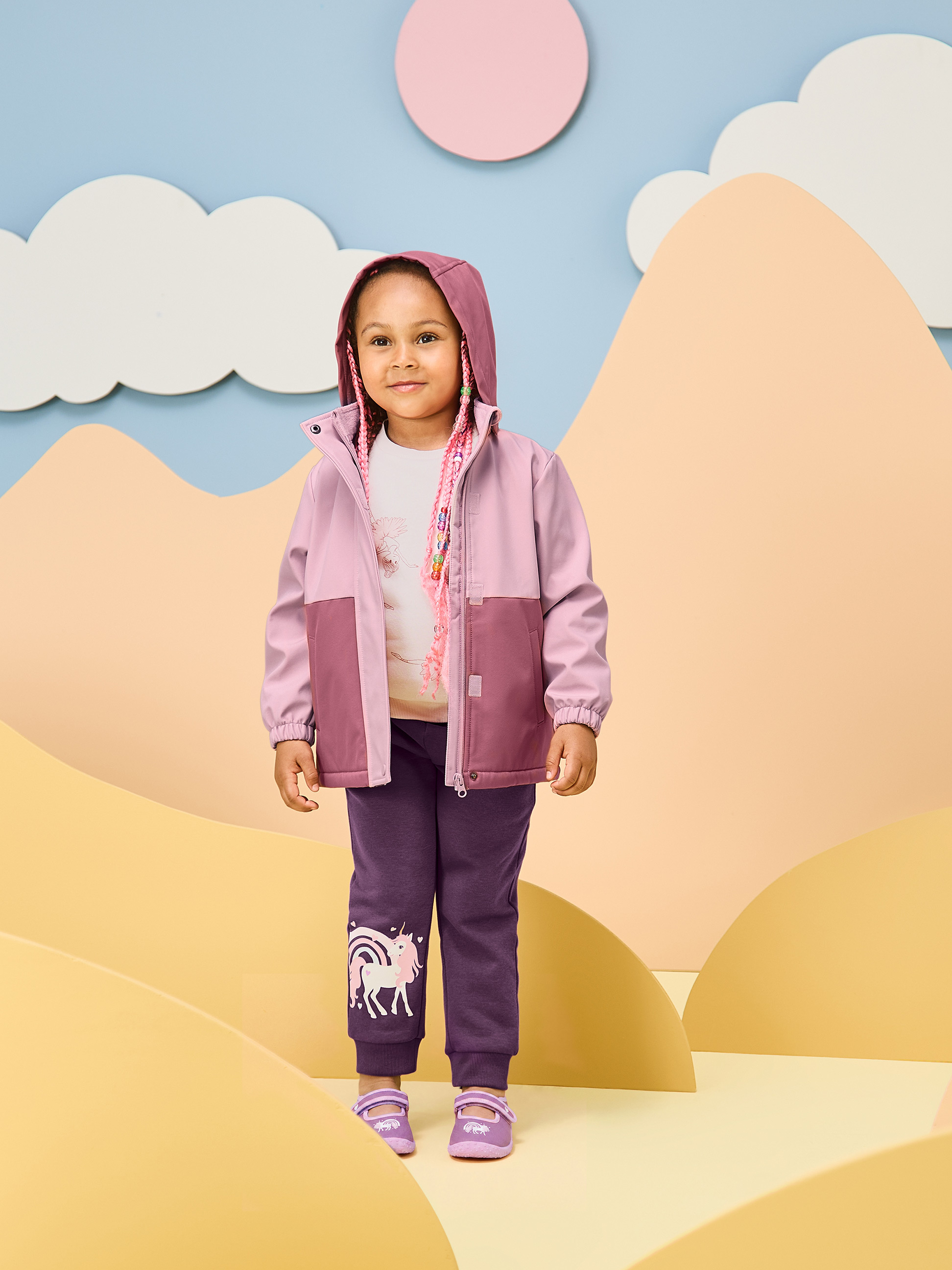 Meisje in roze jas en paarse eenhoornbroek in een speelse omgeving.