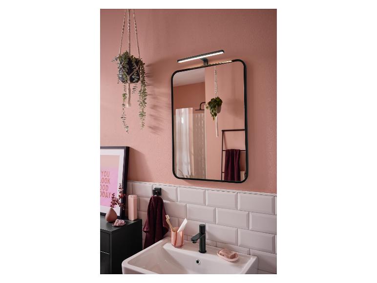 Moderne badkamer met roze muren, een verlichte spiegel, een wastafel en planten.