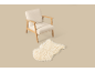 Crèmekleurige fauteuil met houten frame en pluizig vloerkleed op een beige achtergrond.