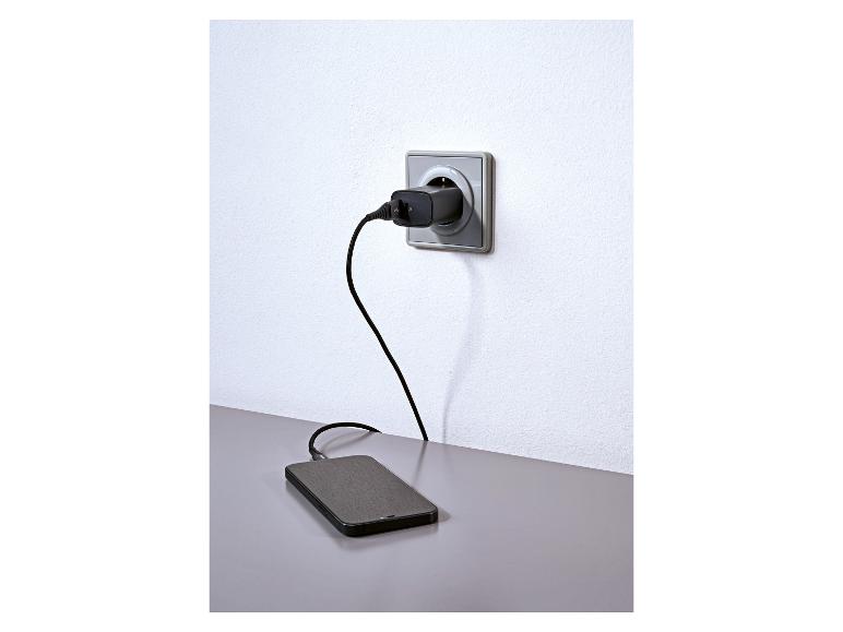 Smartphone wordt opgeladen via een stopcontact met een zwarte oplader en kabel.