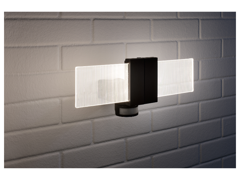 Een moderne zwarte wandlamp met bewegingssensor en LED-verlichting, gemonteerd op een witte bakstenen muur.