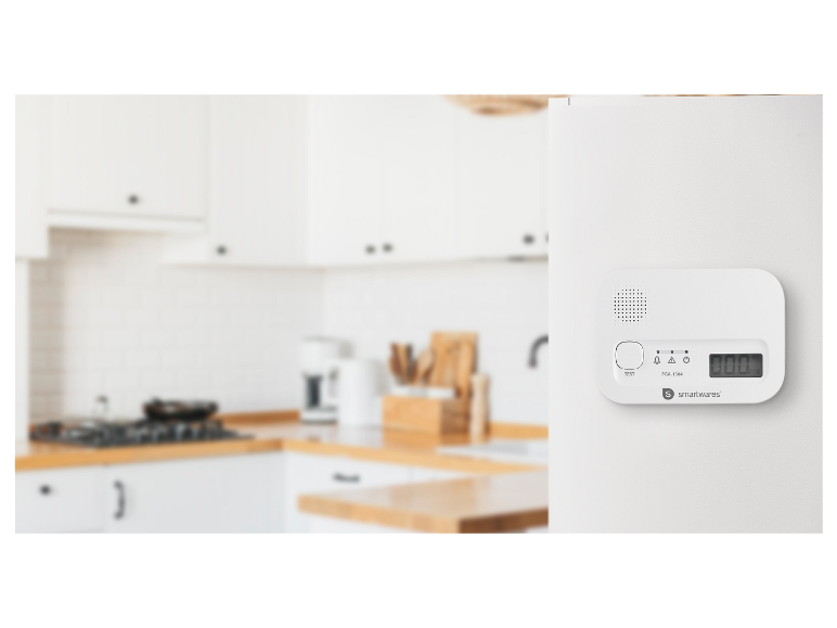 Witte gasdetector met digitaal display en testknop, gemonteerd op een witte muur in een moderne keuken.