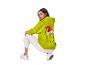 Vrouw gehurkt, draagt een groene Grinch hoodie en een witte broek.