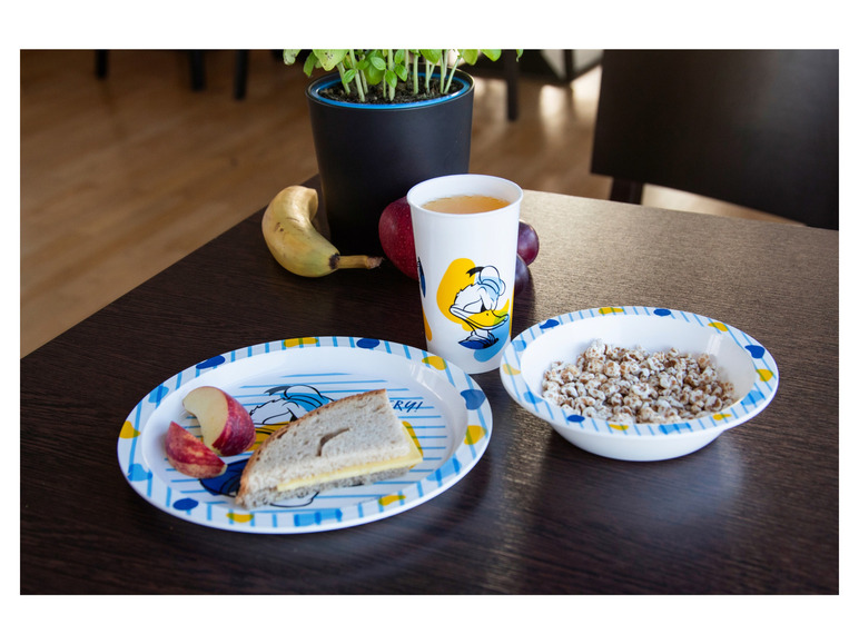 Een bord met een sandwich, appelpartjes en een kom met ontbijtgranen, allemaal met een Donald Duck thema.
