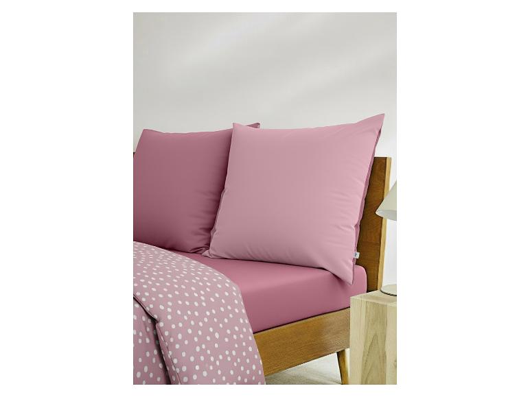 Roze beddengoed met kussens en een wit gestippeld dekbedovertrek op een houten bed.