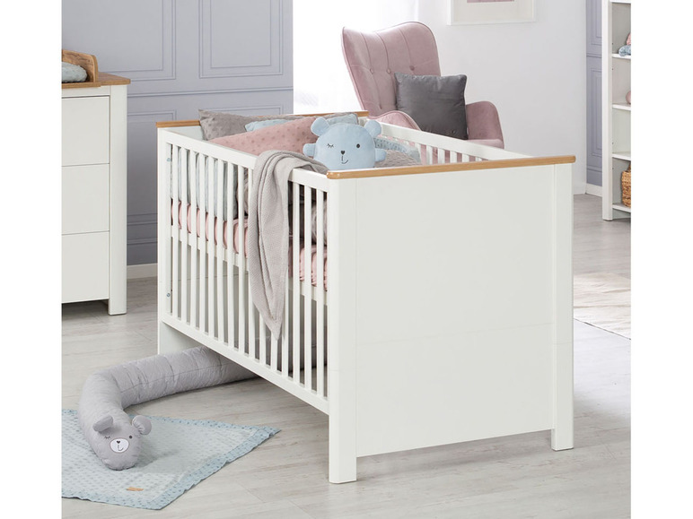 Een wit babybed met houten accenten en een grijze knuffel.