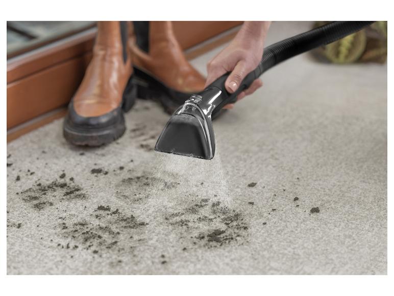 Een persoon reinigt een vuil tapijt met een tapijtreiniger, terwijl hij bruine laarzen draagt.