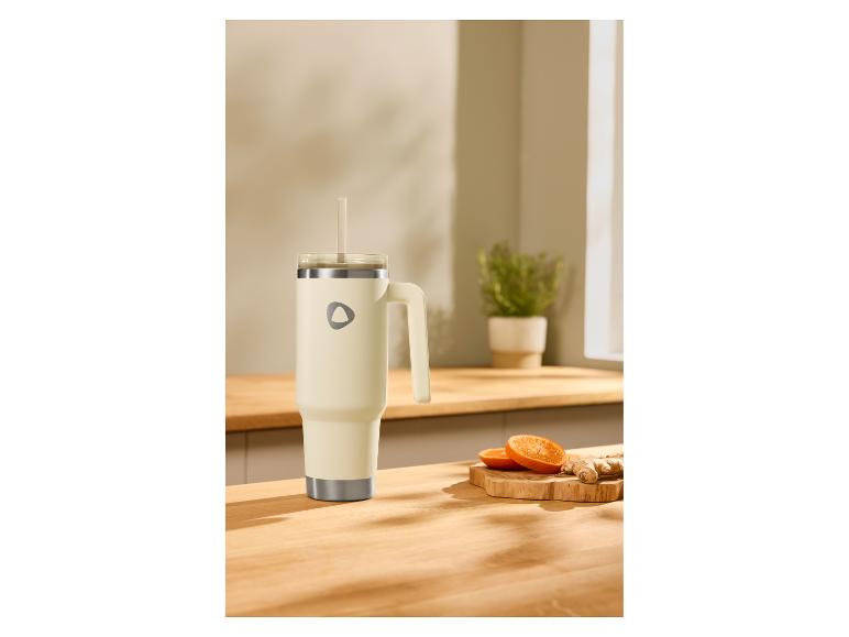Crèmekleurige thermosbeker met handvat en rietje op een houten aanrecht met gember en sinaasappels.