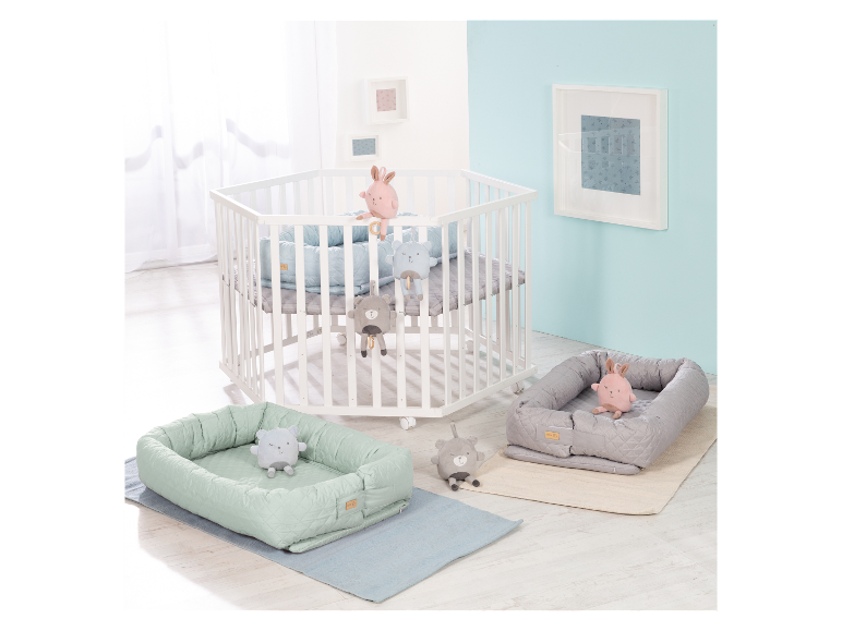 Witte zeshoekige babywieg met matrassen en knuffels.