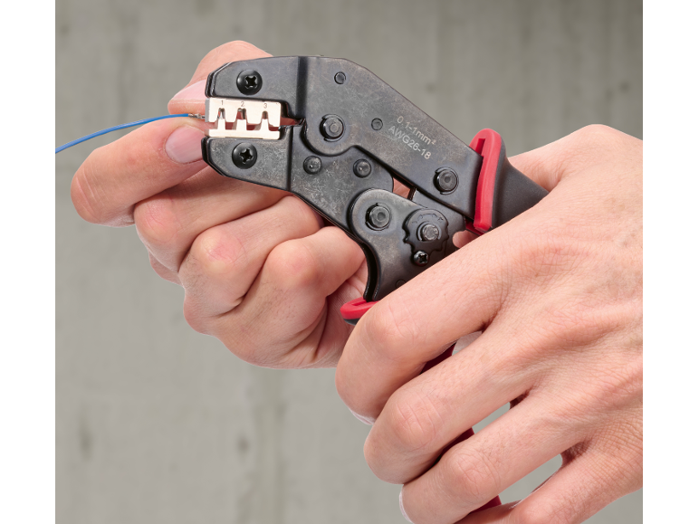 Handen gebruiken een krimptang om een blauwe draad aan te sluiten, met 0.1-1mm² AWG26-18 aanduidingen.