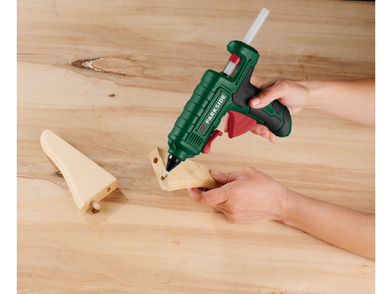 Hand gebruikt een hetelijmpistool op houten stukken op een houten tafel.