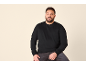 Man in zwarte trui en jeans, glimlachend.