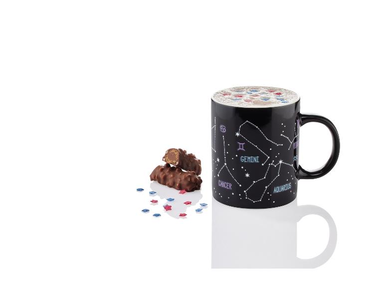 Een zwarte mok met sterrenbeelden, chocolade reepjes en stervormige sprinkles.