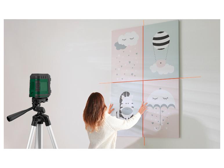 Vrouw gebruikt een laserwaterpas om vier schilderijen aan een muur uit te lijnen.