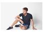 Man in donkerblauw henley shirt en jeans shorts.