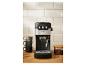 Zwart en zilveren espressomachine op een houten aanrecht met kopjes en koffiebonen.