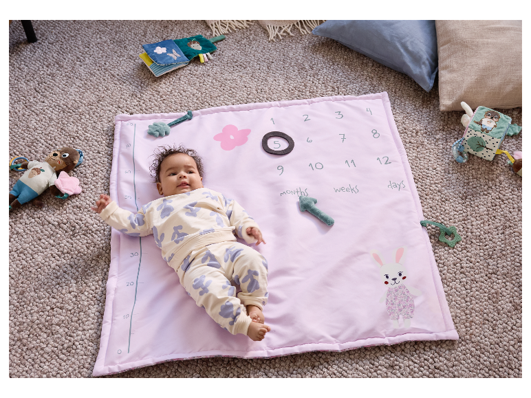 Een baby ligt op een roze speelmat met cijfers en speelgoed.