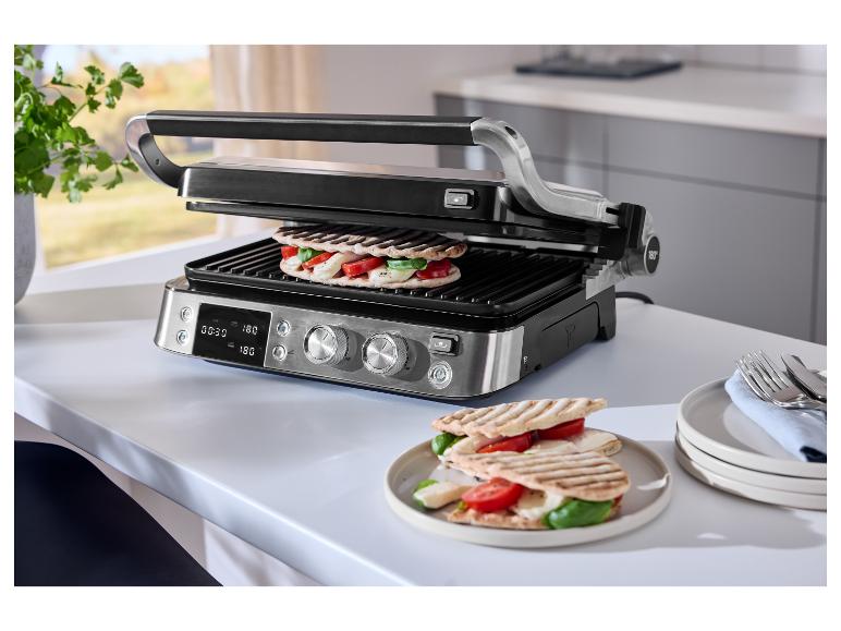 Grill met twee sandwiches, tomaten, mozzarella en basilicum op een witte tafel.