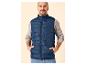 Man in blauw gewatteerd vest en grijze trui, met handen in zakken.