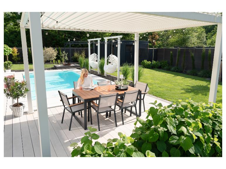 Vrouw leest aan een eettafel op een terras bij het zwembad met een pergola.