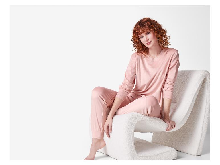 Roodharige vrouw in roze pyjama zittend op een witte stoel.