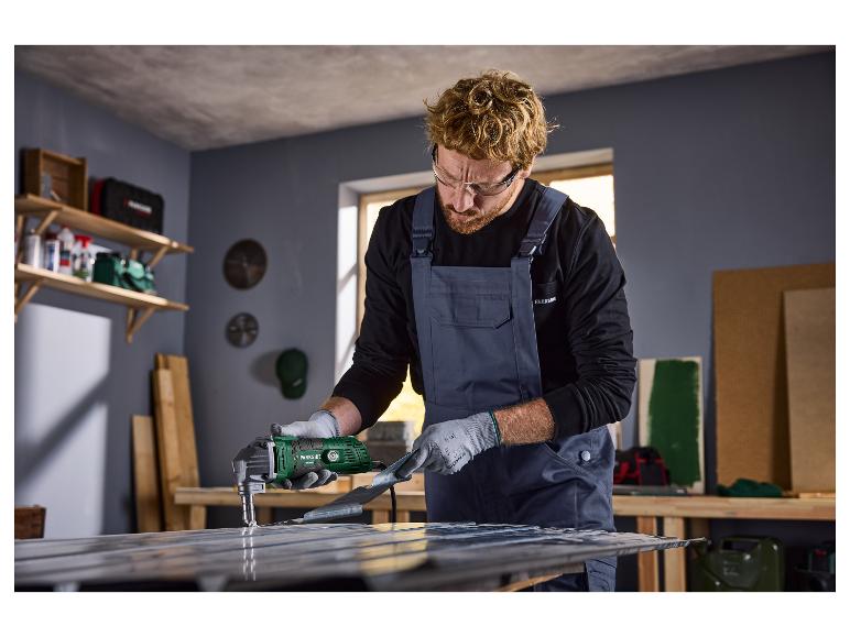 Man met veiligheidsbril en overall gebruikt een Parkside elektrische metaalschaar op een metalen plaat.