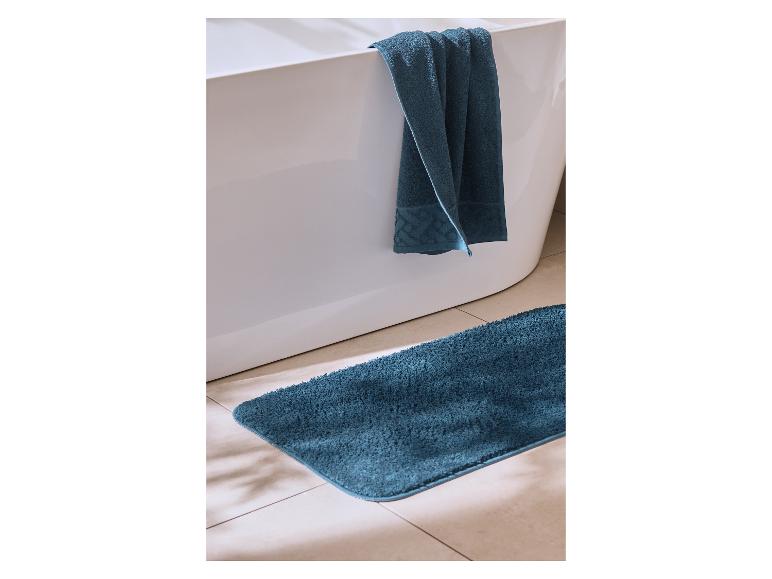 Blauwe handdoek over een badkuip met een bijpassende badmat op de tegelvloer.