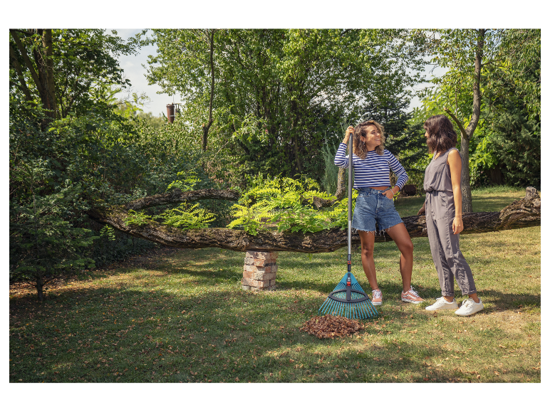Twee vrouwen in een tuin met een hark en bladeren.
