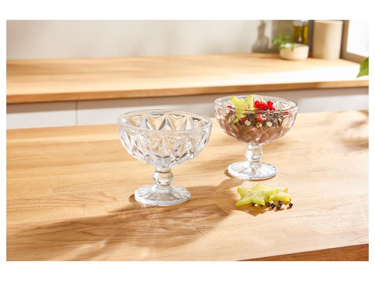 Twee glazen dessertkommen met chocoladedessert en fruit op een houten tafel.